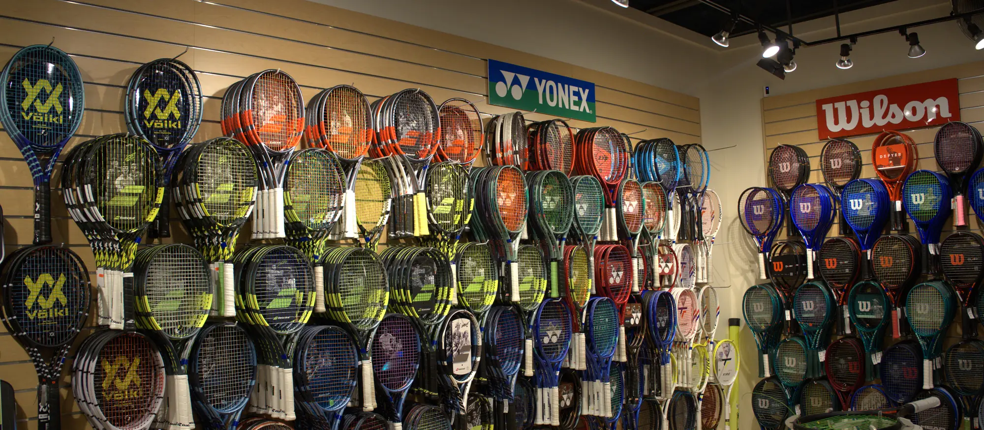 The tennis racquet wall at the Mequon shop, with Yonex, Wilson, Babolat and Völkl frames.