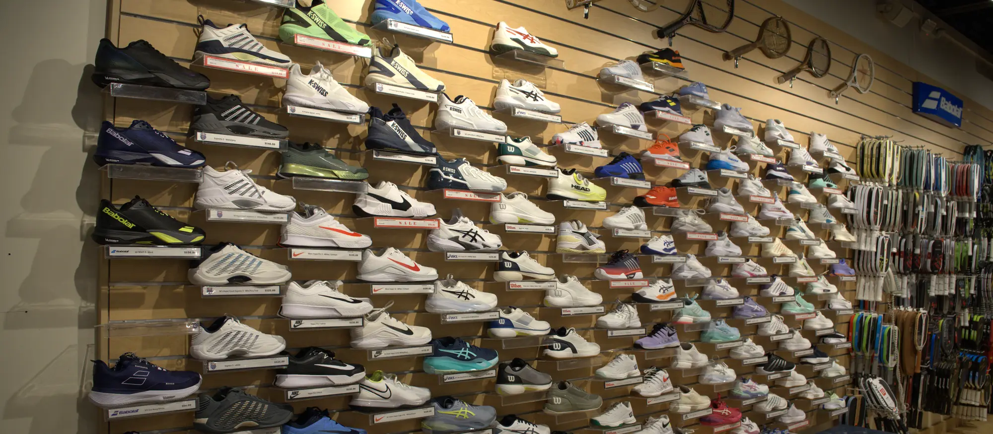 The tennis shoe wall at the Mequon shop, stacked with court shoes from every major brand.