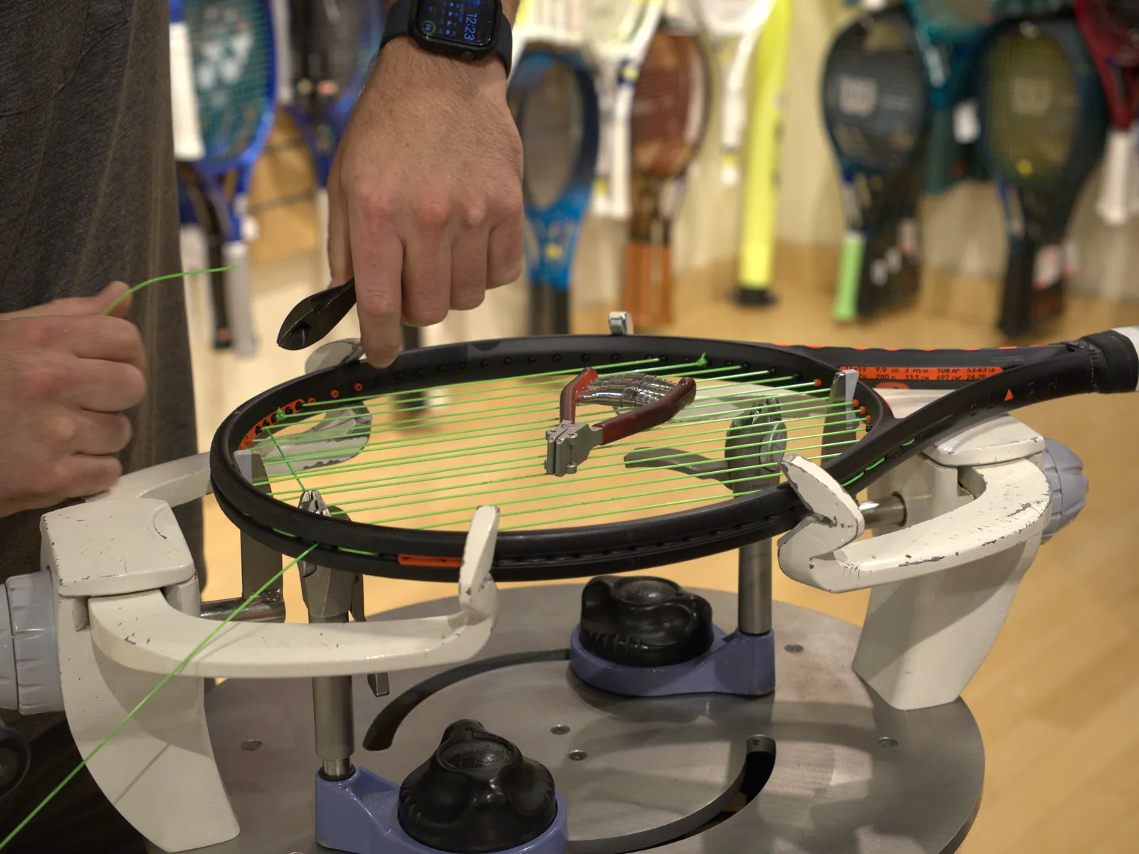 A Les Moise stringer weaving green string into a racquet on the stringing machine at the Mequon shop.